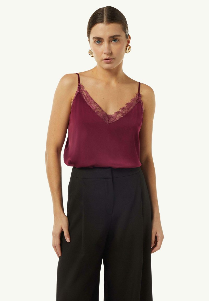 Burgundy satin camisole with lace trim at the neckline, thin straps, paired with high-waisted black trousers. Smooth texture, elegant design.
