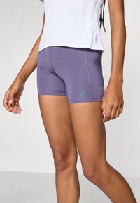 Lilla sportshorts med et tætsiddende design, glat tekstur og stikninger. Har et Adidas-logo på den nederste venstre side.