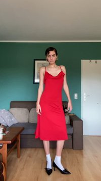 Vestido vermelho com alças spaghetti, decote drapeado, tecido suave, até ao joelho, combinado com sapatos de salto alto pretos e meias brancas.