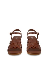 Barna bőrből készült női szandálok fonott elülső pántokkal, bokánál csattal rögzítve, lapos talppal, elölről nézve.