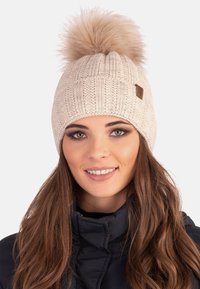 Caciulă tricotată de culoare bej deschis, cu o textură ribb, având un pompon mare din blană artificială în vârf; prezintă un mic etichetă cu logo din piele maro.