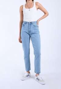 Ljusblå högmidjade jeans med tapered ben, tillverkade av denim, kombinerade med en figurnära vit linne och vita sneakers med marinblå detaljer.