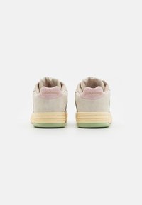 Sneaker beige in suede con un sottotacco rosa chiaro, una intersuola gialla e una suola verde. Presenta il logo "Saucony" sul tallone.