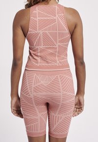 Åtsittande träningsset i dämpad rosa med geometriska mönster. Topp med rundad halsringning och kortbyxor som är knälånga med matchande detaljer.