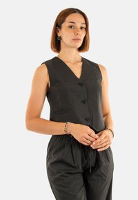 Gilet senza maniche grigio scuro con scollatura a V profonda, tre bottoni e una tasca frontale. Il tessuto strutturato ha righe verticali.