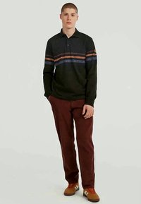 Μακρυμάνικη σκούρα πράσινη πόλο μπλούζα με οριζόντιες ρίγες σε πορτοκαλί και μπλε, σε συνδυασμό με μπορντό παντελόνι και καφέ αθλητικά παπούτσια.