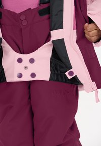 Bordeaux winteroutdoor kleding met een roze en zwarte design. Voorzien van drukknoopsluitingen, elastische taille en branding aan de linkeronderzijde.