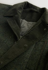 Herringbone patterned wool jacket in dark green with a corduroy collar, zip closure, and gray lining, featuring snap buttons and pockets.
