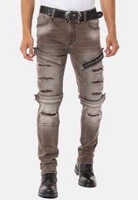 Abgewetzte graue Denim-Jeans mit mehreren Rissen; schlanke Passform, zusätzliche Taschen und ein schwarzes Logo-Patch am Oberschenkel.