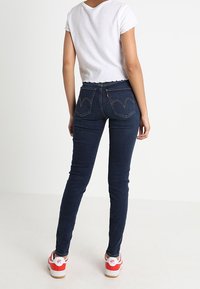 Smal mörkblå jeans med medelhög midja, med bakfickor med en distinkt böjd söm. I kombination med en vit kortärmad t-shirt och sneakers med röda accenter.