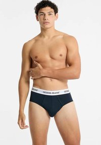 Slip in cotone nero con una fascia bianca recante il logo "GUESS JEANS". Texture liscia con un taglio classico e design supportivo.