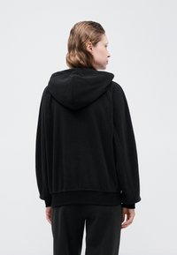 Svart hettegenser med avslappet passform, med hette, ribbede ermer og teksturert stoff. Designet har en jevn finish og subtile sømmer.