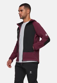 Veste à capuche bordeaux et noire avec fermeture éclair à l'avant, poches latérales et détail de logo sur la manche. Fabriquée en tissu texturé et durable.