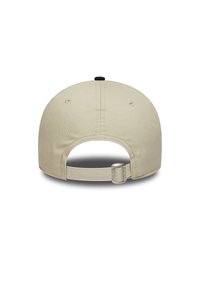 Beige pet met een ronde vorm, een zwarte knop bovenop, en een verstelbare strap aan de achterkant met een zilveren hardware accent.