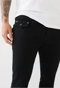Jeans negre din denim cu un croi slim, având cinci buzunare, închidere cu nasture metalic și detalii subtile de cusătură pe buzunarele din spate.