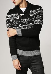 Pull noir en maille avec un motif géométrique gris sur la poitrine, col châle et poignets et ourlet côtelés gris.