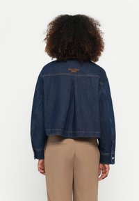 Donkerblauwe spijkerjacket met een cropped ontwerp, met oranje geborduurd merkteken op de achterkant en knoopmanchetten.