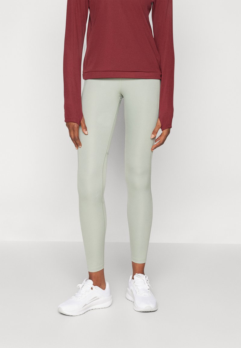 Világoszöld leggings, rugalmas anyagból készült, egy bordó hosszú ujjú felsővel párosítva. Fehér sportcipő egészíti ki az összeállítást.