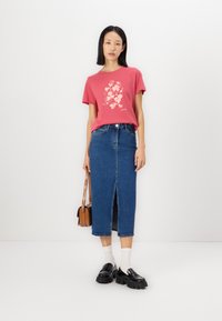 Röd T-shirt med blommönster, kombinerad med en lång denimkjol med slits framtill. Svarta plattformsskor och en liten brun handväska.