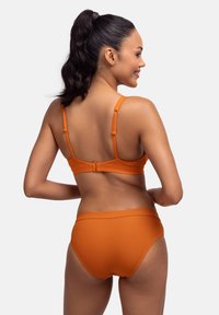 Oranžs ribots bikini komplekts ar regulējamiem siksniņām un aizdares slēgšanu aizmugurē. Apakšdaļa ir augstiem jostasvietas dizainā.