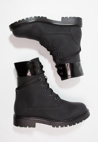 Svarta ankelstövlar med matt finish, med en blank svart detalj upptill, snörning och grov mönstrad sula.