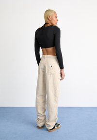 Zwarte cropped langemouwen top met een strikdetail aan de achterkant, gecombineerd met lichtbeige wijde broekspijpen met twee achterzakken en een logo op het zak.
