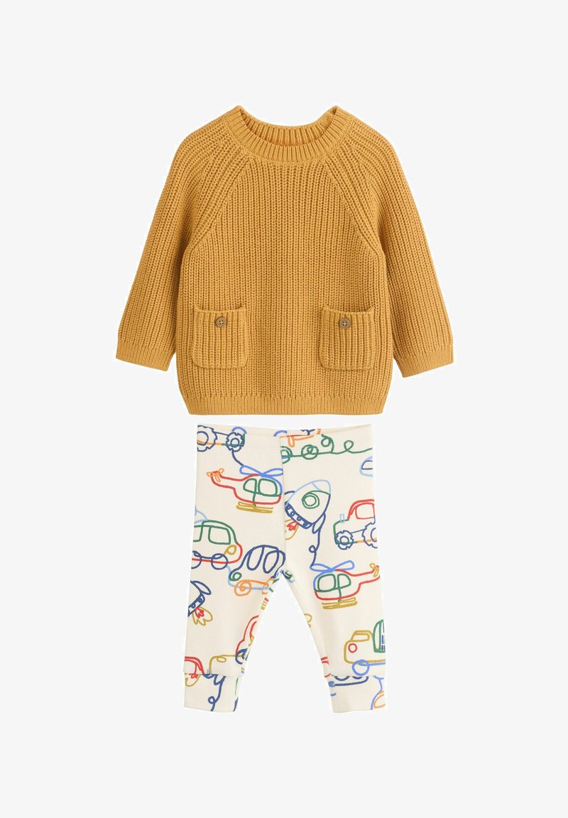 Knit sweater in mustard with ribbed texture and two pocket details; paired with cream leggings featuring colorful, illustrated vehicle patterns.