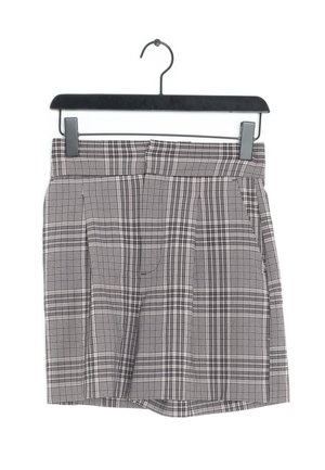 Grijze en zwarte geruite rok met plooien, gemaakt van geweven stof. Heeft een tailleband en hangt aan een zwarte plastic hanger.