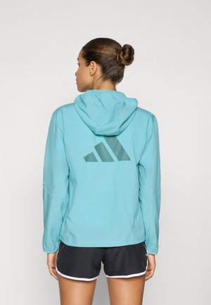 Light blue hooded jacket with a smooth texture and a large dark green Adidas logo on the back. Features long sleeves and elastic cuffs.