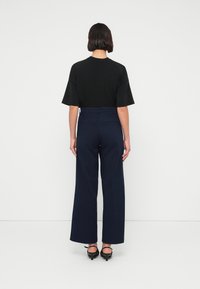 Μαύρο τοπ με κοντά μανίκια και ψηλόμεσο παντελόνι σε σκούρο μπλε χρώμα με φαρδιά πόδια. Το ύφασμα φαίνεται λείο, με τσέπες στην πλάτη και παπούτσια με χαμηλό τακούνι.