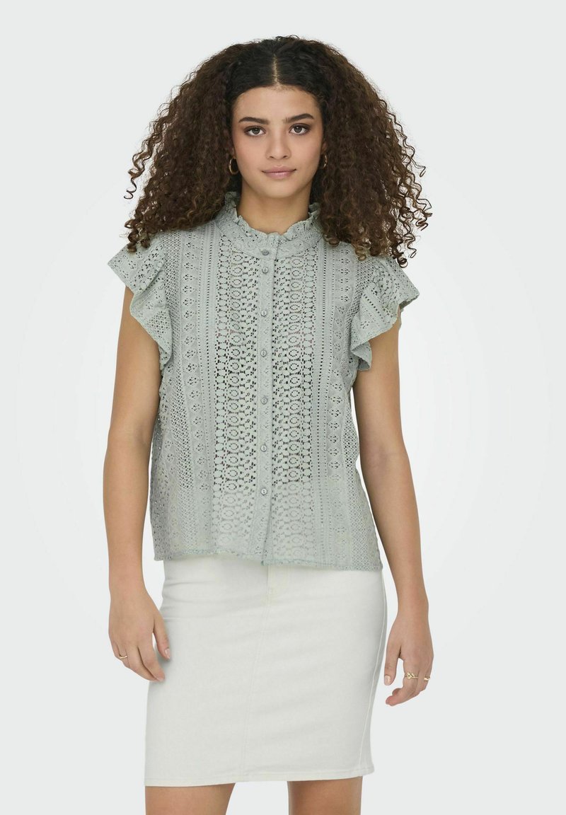 Lichtgroene blouse met korte mouwen, voorzien van een kantpatroon, gerimpelde mouwen, knoopsluiting en een gekartelde kraag, gecombineerd met een witte rok.