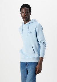 Gaiši zils kapuce ar priekšējo kabatu un aukliņu kapuci. Iezīmēti riboti aproces un apakša, ar logo izšuvumu uz krūšu zonas.