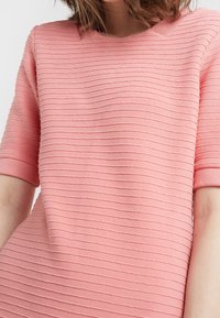 Tričko s krátkým rukávem z jemného růžového materiálu, s texturovanými pruhy a kulatým výstřihem. Normální střih s hladkým povrchem.