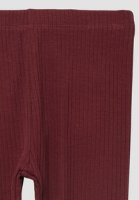 Tissu côtelé bordeaux profond avec une ceinture élastique et un détail de couture visible, probablement une partie de leggings ou pantalons ajustés.