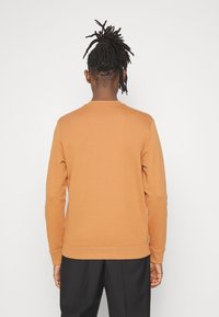 Sweatshirt in verbranntem Orange, aus weichem Stoff, mit Rundhalsausschnitt und langen Ärmeln. Gerippte Bündchen und Saum für eine enge Passform.