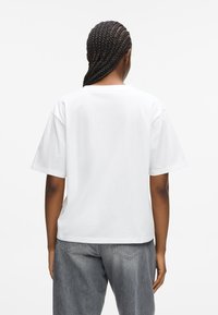 T-shirt bianca in cotone con una vestibilità comoda, collo rotondo e maniche corte. Indossata con pantaloni in denim grigi, caratterizzati da un design semplice e pulito.