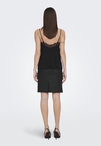 Top nero senza maniche con dettagli in pizzo sul retro, abbinato a una gonna in pelle nera aderente e scarpe con tacco alto nere.
