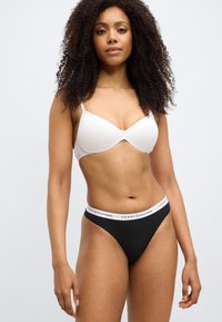 Λευκό ενισχυμένο σουτιέν και μαύρο στρινγκ με λευκή ζώνη μέσης που φέρει το λογότυπο "TOMMY HILFIGER". Λείο υλικό και μίνιμαλ σχεδιασμός.