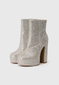 Botas de tobillo plateadas con plataforma cubiertas de pequeños rhinestones reflectantes y tacones gruesos sobre un fondo sencillo.
