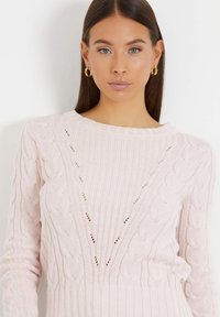 Jersey de punto rosa claro con patrones de cable, cuello redondo acanalado y mangas largas. Presenta un diseño texturizado con acentos de calado.