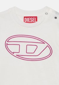 Balta medvilninė marškinėliai su dideliu rožiniu "Diesel" logotipo dizainu, apvaliu iškirpimu ir spaudinukų akcentais ant peties.
