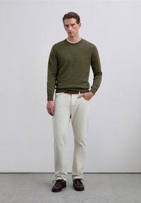 Sweter w kolorze oliwkowej zieleni, kremowe spodnie i brązowe buty. Sweter jest dziany, spodnie gładkie. Buty mają sznurowadła i teksturowaną podeszwę.