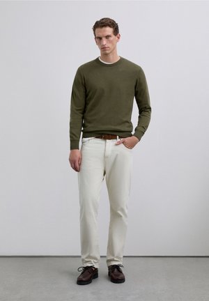 Olivově zelený svetr, krémové kalhoty a hnědé boty. Svetr je pletený, zatímco kalhoty jsou jednoduché. Boty mají tkaničky a texturovanou podrážku.