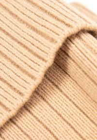 Beige gebreide stof met een geribbelde textuur, met gebogen plooien en zachte garen, die warmte en comfort benadrukt.