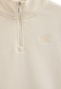 Polo de forro polar color crema con cuello con cremallera, que presenta una tela texturizada y un logotipo cuadrado en relieve "POLO CLUB" en el pecho.