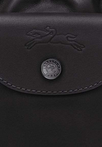 Schwarze Lederhandtasche mit einem geprägten Logo eines sprungbereiten Hundes, einem runden silberfarbenen Hardware-Akzent und kontrastierenden Nähten entlang der Kante.