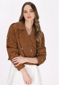 Ruskea mokkanahkainen kaksirivinen takki, jossa on suuret läpät, nappiyksityiskohdat ja käännetyt hihansuut. Sujuva texture ja lyhennetty malli.