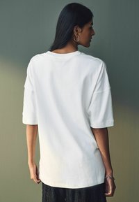 Witte oversized t-shirt met korte mouwen, voorzien van een ronde hals, een soepele textuur en een relaxte pasvorm. Minimalistisch ontwerp zonder patronen.