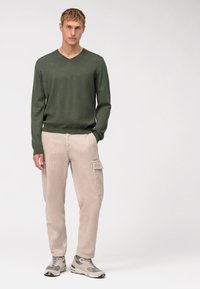 Olijfgroene v-hals sweater, roomkleurige ribfluweel cargobroek met zakken, en grijze sneakers met groene accenten. Eenvoudig ontwerp en ontspannen pasvorm.