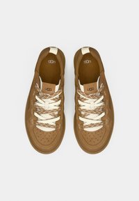 Καφέ σουέντ αθλητικά παπούτσια με κρέμ κορδόνια σε σχέδιο διαμαντιού, κυκλικές περφορέ στο μπροστινό μέρος και το λογότυπο 'UGG' στη γλώσσα.